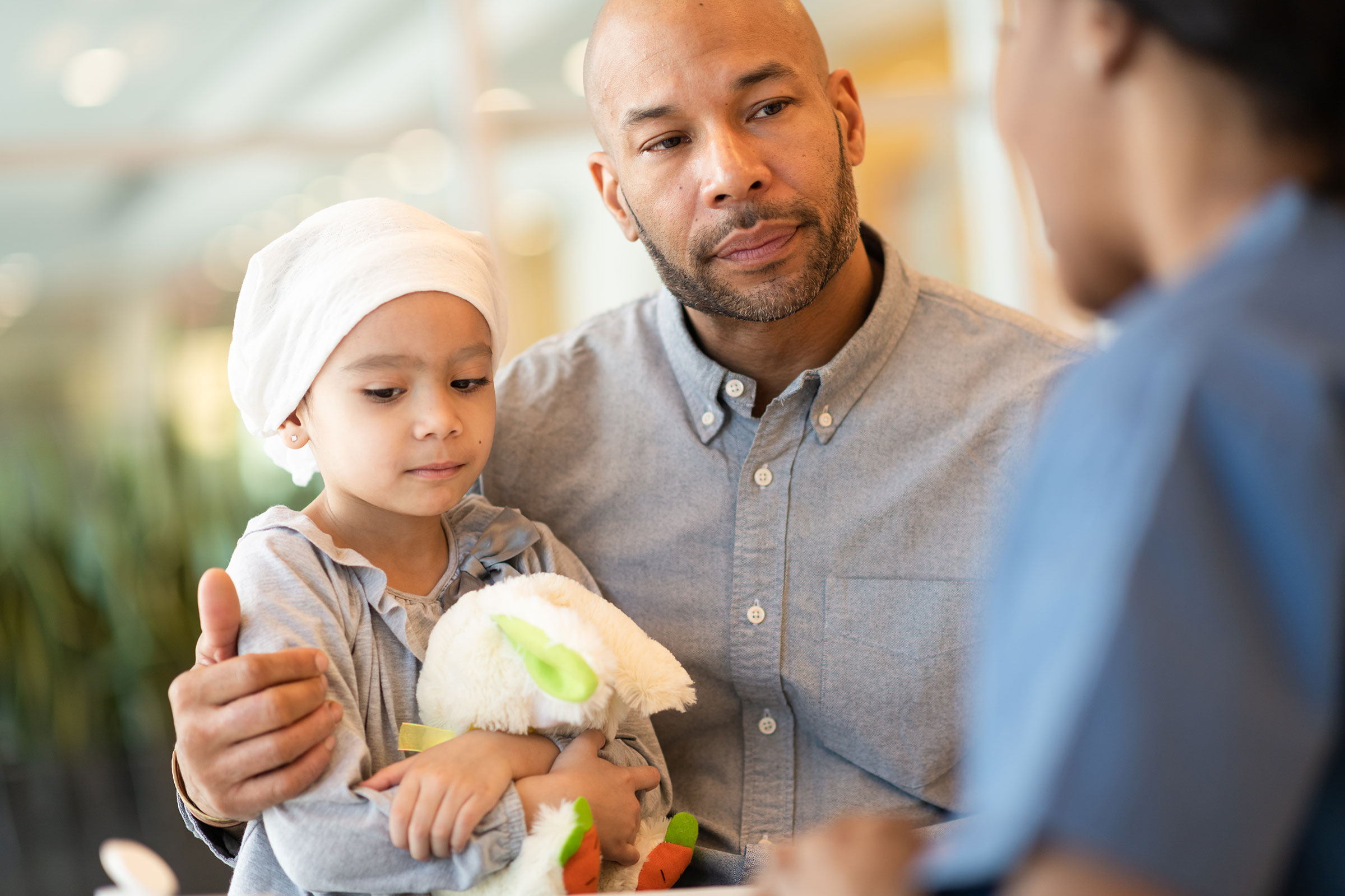Young child with cancer and her father talk to a doctor.
