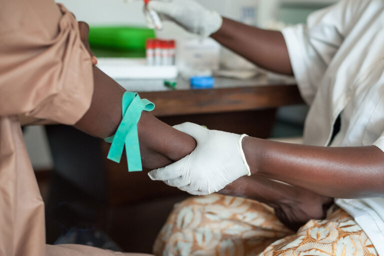 A gloved nurse prepares to draw blood from a patient.