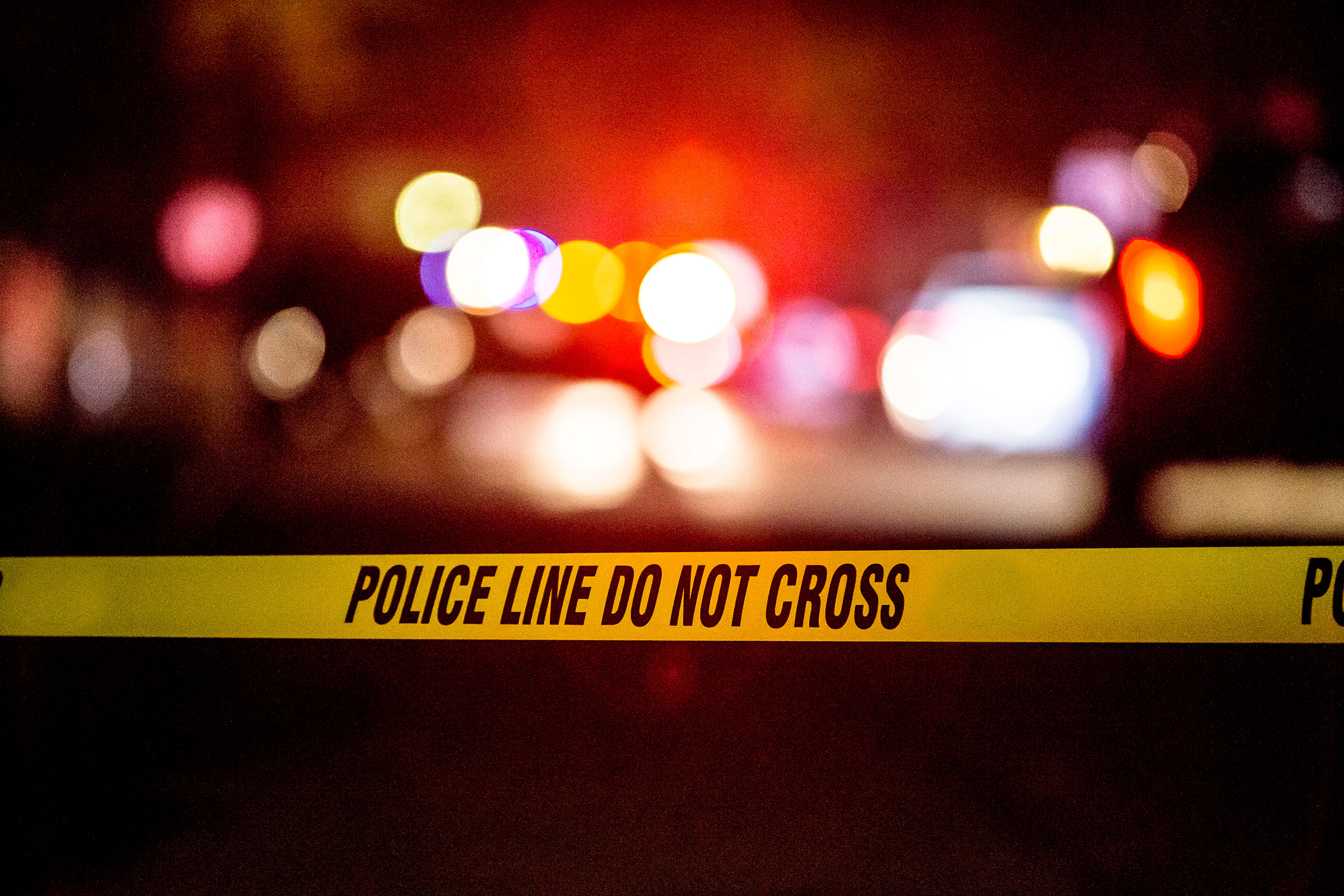 Image of a crime scene, with blurry police lights and yellow tape with "police line do not cross"