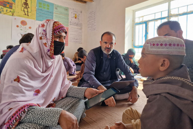 A woman and man sit on the floor with a primary-school aged child in a school in Afghanistan