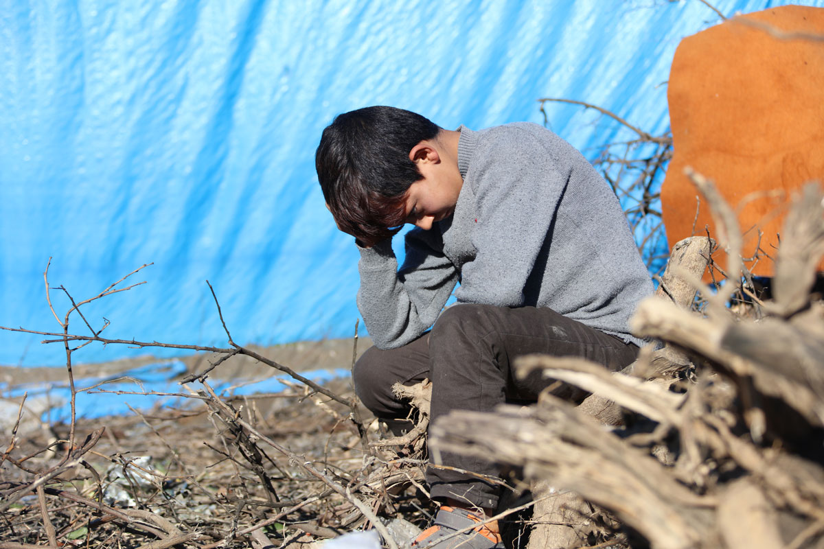 Young sad boy in refugee camp, head bowed.