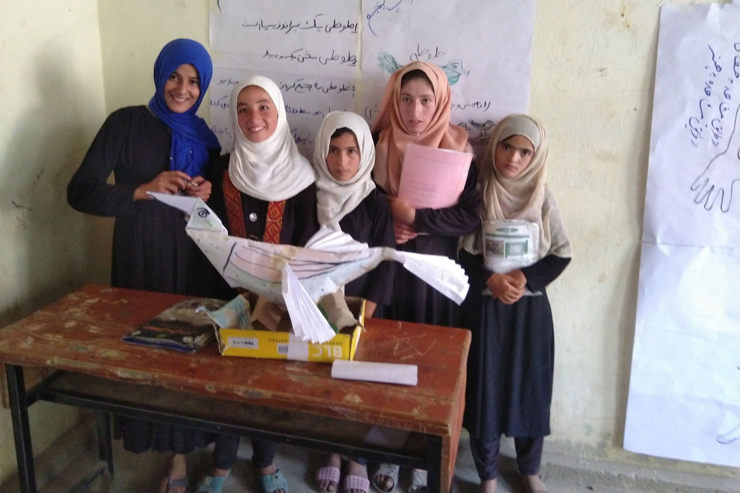 Five primary school girls stand behind a paper model of a bird .