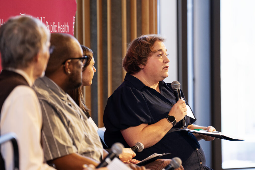 A woman holds a microphone and speaks as part of a panel discussion