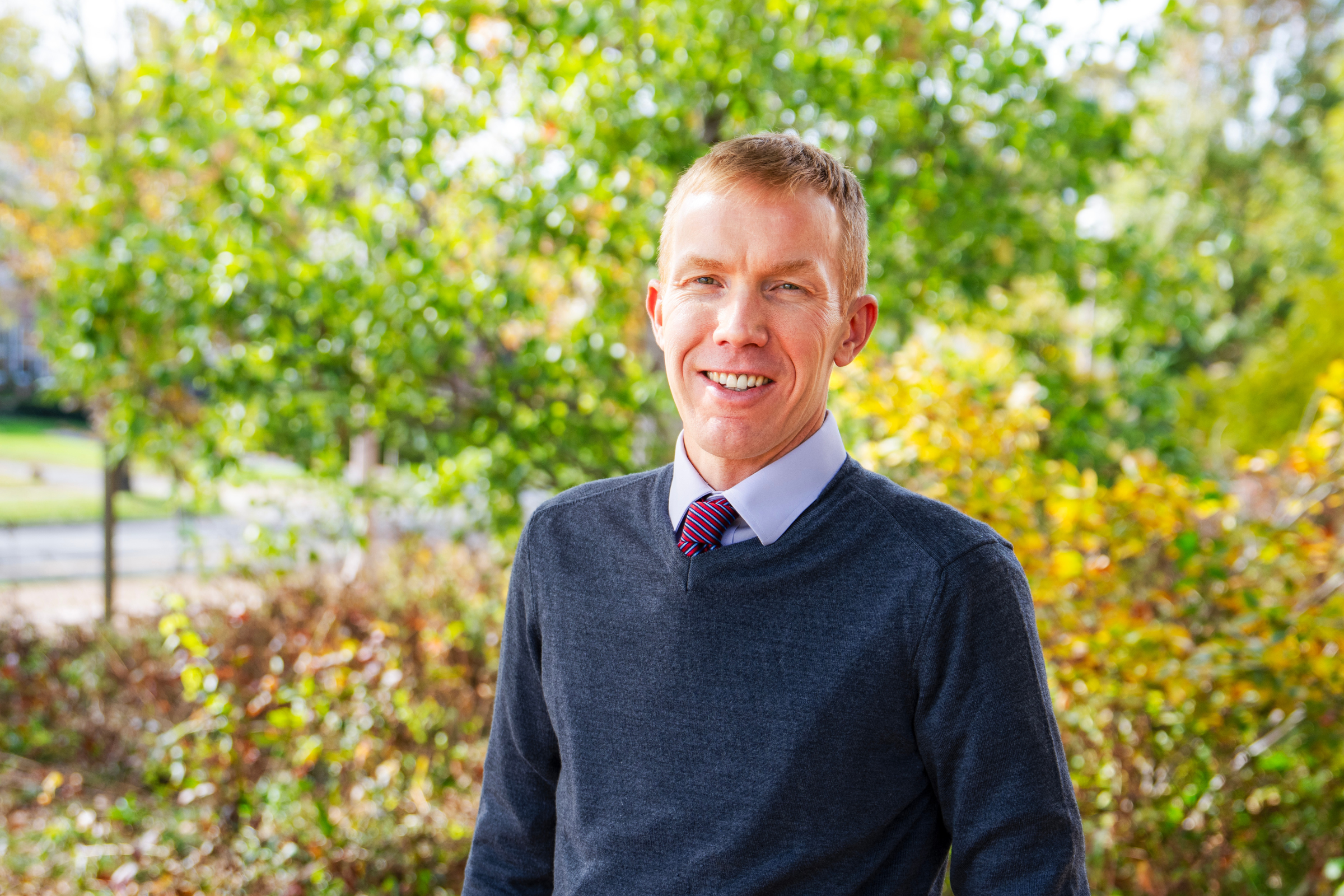 photo of faculty member derek brown in a blue sweater, outside, smiling for the photo