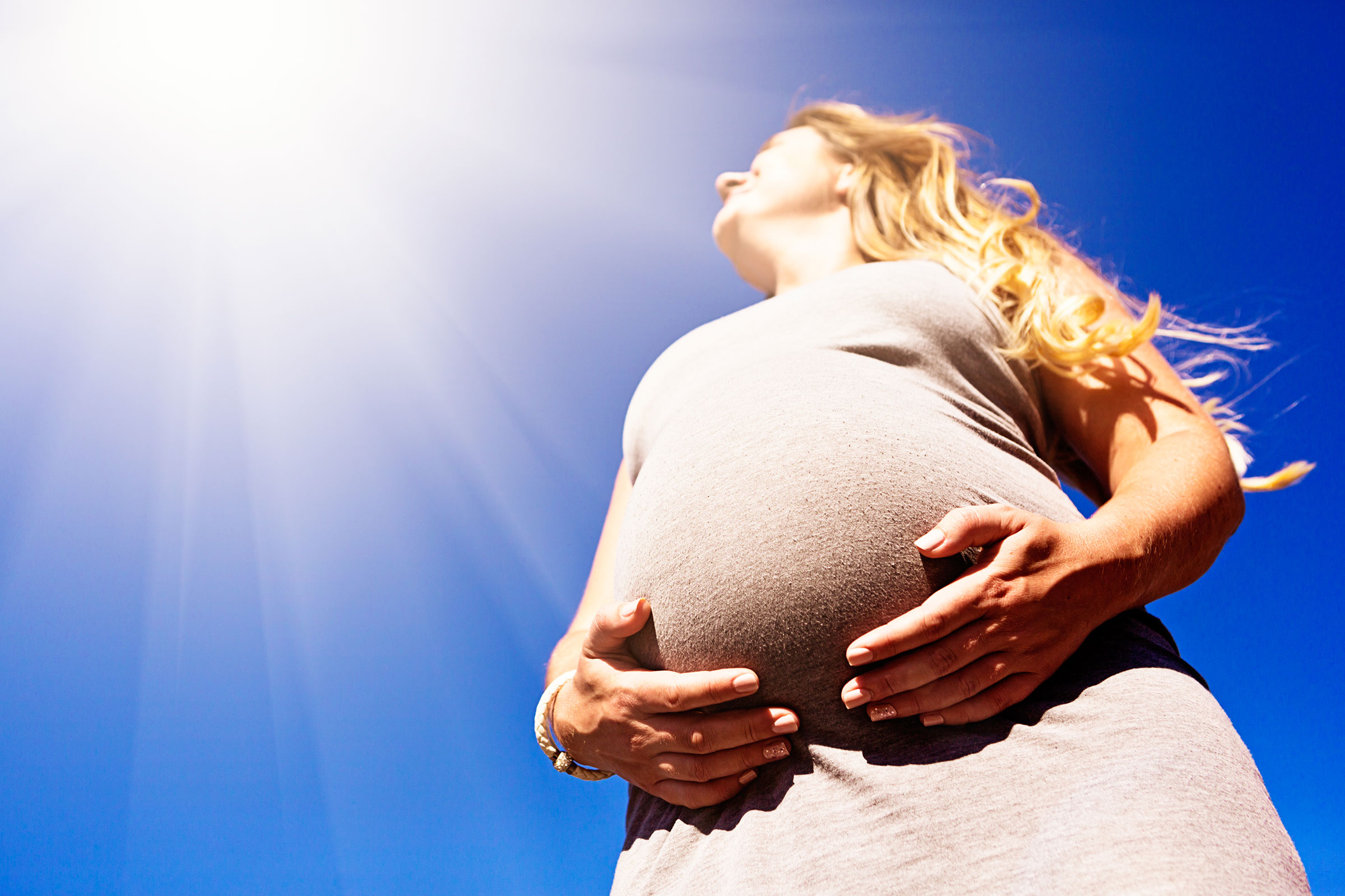 Pregnant woman with her hand on her belly and the sun appearing above, indicating a hot, bright day